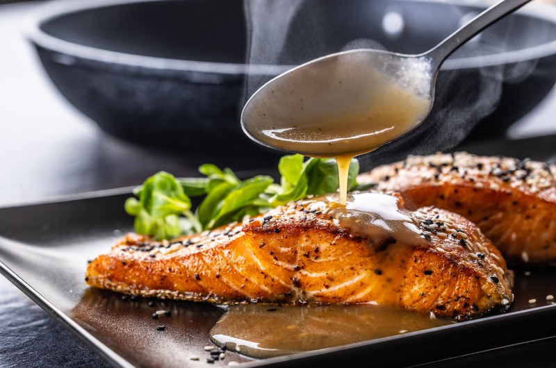 spoon finishes portion by pouring demiglas sauce salmon fillets